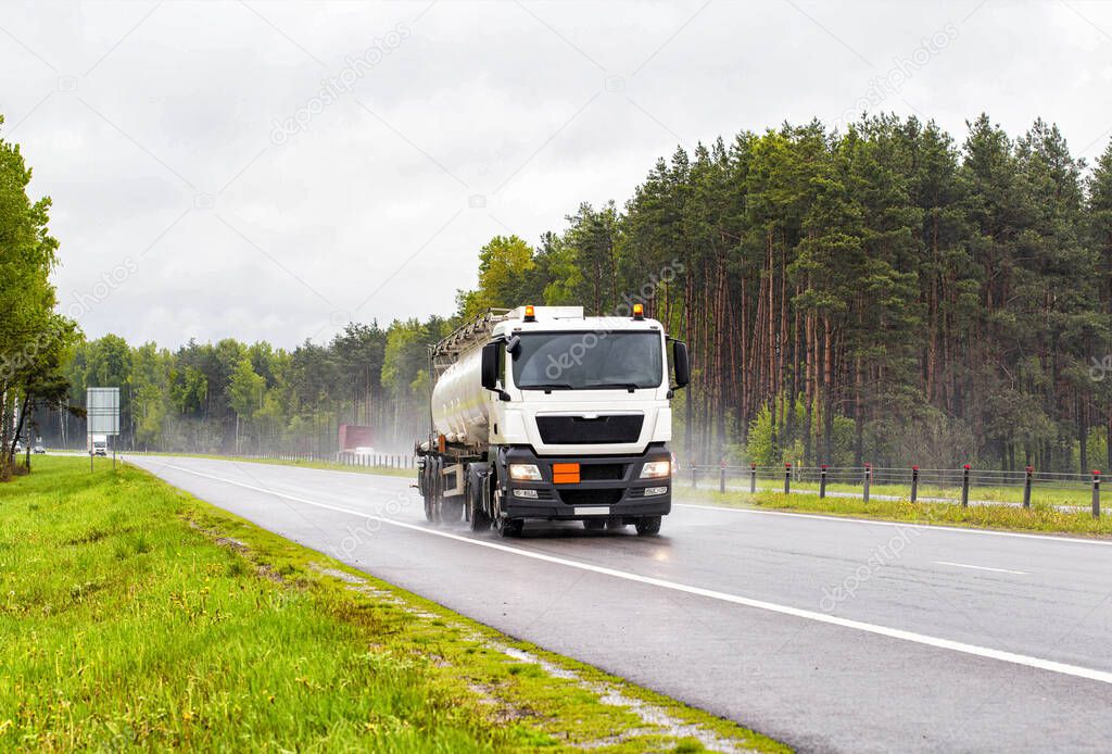 A special vehicle for the transport of explosive substances travels along the road and transports oil products in rainy weather. Concept of the industry and transportation of petroleum products from producer to consumer. Headlights