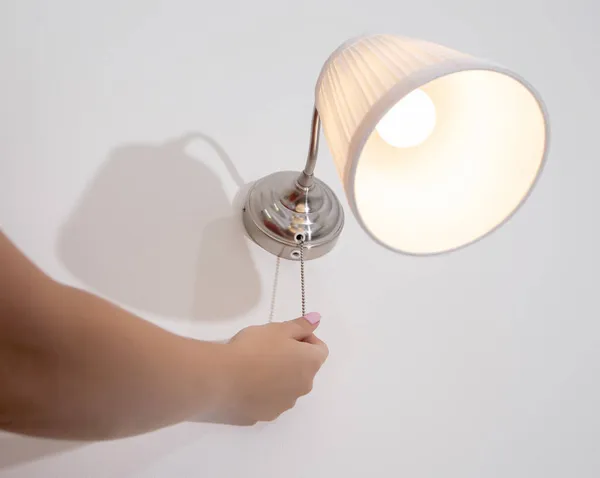 Uma mão de mulher liga e desliga a parede com uma corda. Luz noturna acima da cama, close-up — Fotografia de Stock