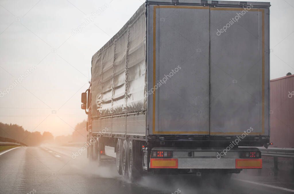 A semi-trailer truck drives on a wet road during poor visibility and rain. Bad foggy and rainy weather. Copy space for text