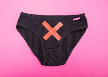 Pembe arka planda kırmızı haçlı siyah kadın külotu. Kadın jinekolojik hastalıklar, boyun erozyonu ve polisistik yumurtalık kavramı, yakın plan.