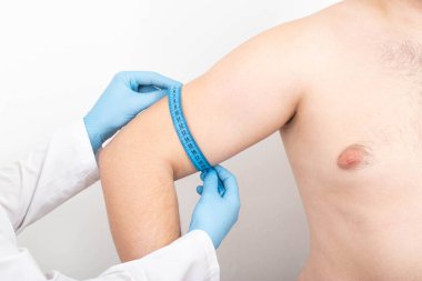 Doktor, trisepslerin estetik cerrahi ile büyütülmesi için bir mezura ile bir adamın trisepslerini ölçer.
