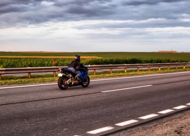Spor motosikletli bir motorcu yazın bir otoyolda gökyüzündeki bulutların arkasına doğru yol alır.