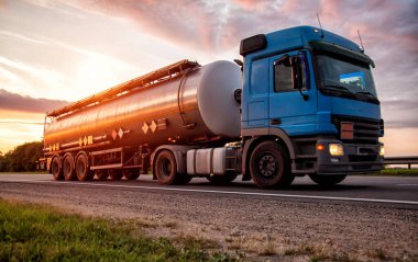 Yarı karavan tankerli mavi modern bir kamyon, tehlikeli malları akşam güneşinin arka planına taşıyor. Sıvı kargo taşıma konsepti, risk sınıfı ADR.