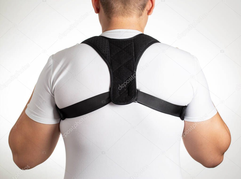 A man in a white T-shirt with a black posture corrector on a white background. Back pain and problem correction concept