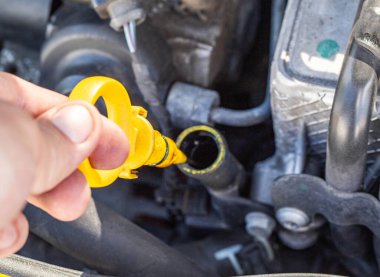 Bir adamın eli, motor yağı seviyesini ve kalitesini kontrol etmek için dizel bir arabanın motorundaki yağ çubuğunu çıkarır. Yağ değiştirme servis aralığı