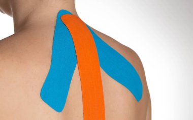 Kızın boynunu ve omuzlarını mavi ve turuncu kineziyolojik bantla bantlıyorum. Alternatif tıp, kas ve bağ dokusu eğitimi, yakın çekim.