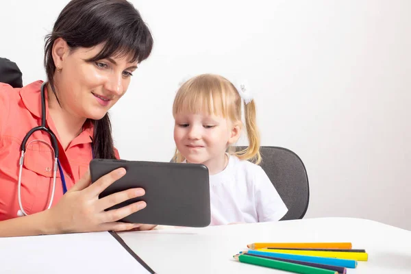 El médico pediatra le muestra una tableta a una niña. Tratamiento de los niños. Copiar espacio para texto —  Fotos de Stock