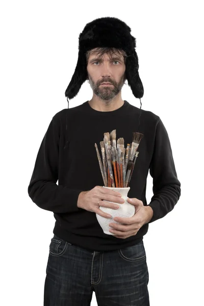 Man in hat ear flaps holding jug with brushes — Stock Photo, Image