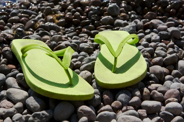 Chinelos verdes na praia de seixos — Fotografia de Stock