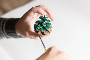 Yeni yıl el sanatları. Çocuk çam kozalağı boyuyor..