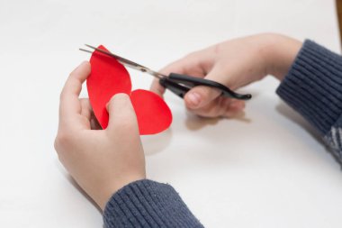 Çocuk beyaz bir arkaplanda Sevgililer Günü için kalp kesiyor.