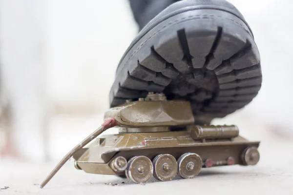 An army boot steps on a damaged toy tank. War in Ukraine, destruction of the civilian population