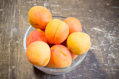 Tahta bir masadaki kasede taze kayısılar.