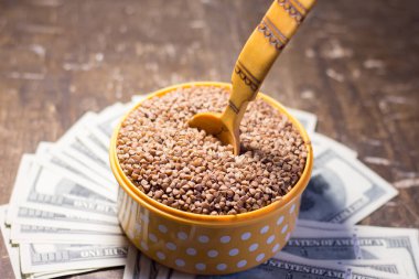 Buckwheat in a bowl with a wooden spoon on dollar bills. Rising prices in Ukraine due to the war