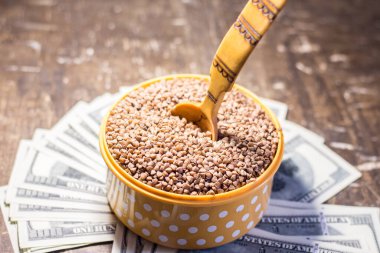 Buckwheat in a bowl with a wooden spoon on dollar bills. Rising prices in Ukraine due to the war