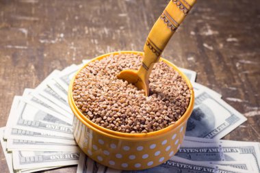 Buckwheat in a bowl with a wooden spoon on dollar bills. Rising prices in Ukraine due to the war