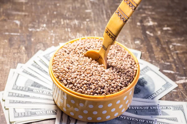 Buckwheat in a bowl with a wooden spoon on dollar bills. Rising prices in Ukraine due to the war