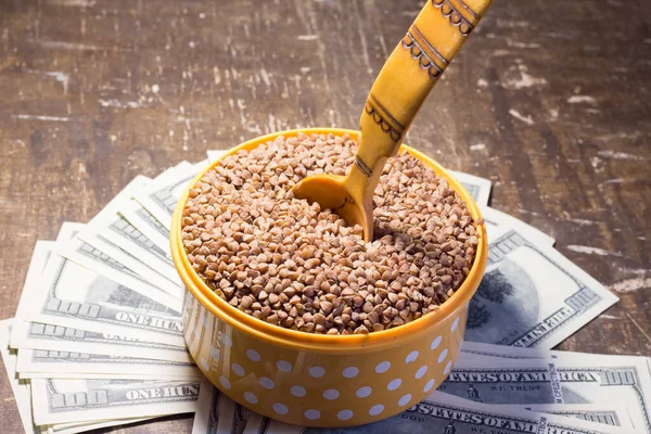Buckwheat in a bowl with a wooden spoon on dollar bills. Rising prices in Ukraine due to the war