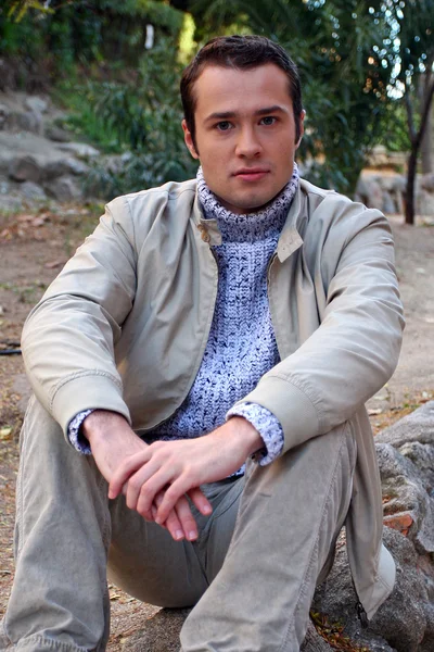 Model młody mężczyzna siedzi na kamieniu i wygląda prosto do aparatu — Zdjęcie stockowe