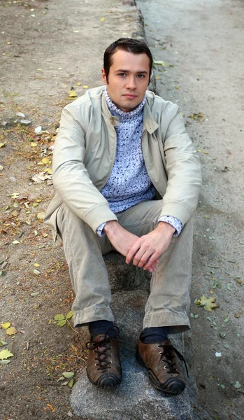 Young male model sits on the stones and poses for the camera — Stock Photo, Image