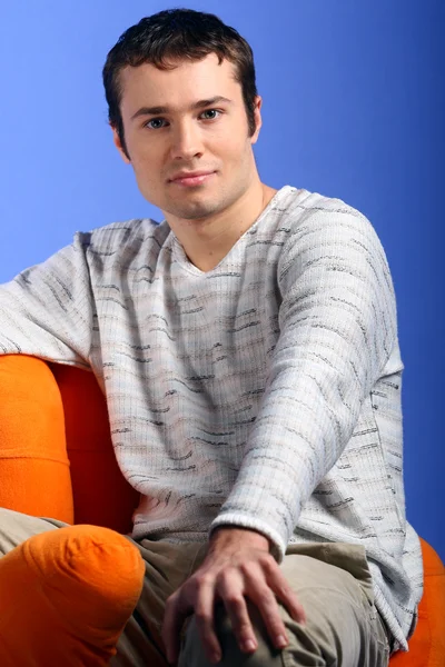 Young male model sits in the orange chair isolated on blue — Stock Photo, Image