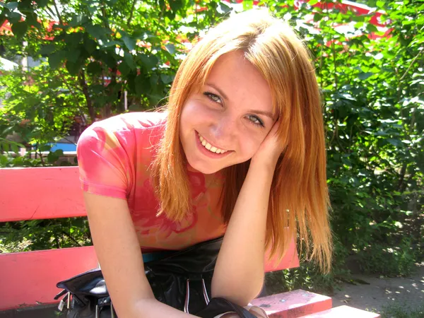 Hermosa chica sonríe y posa en un banco — Foto de Stock