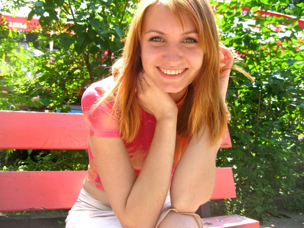 Beautiful girl smiles and poses on a bench — Stock Photo, Image