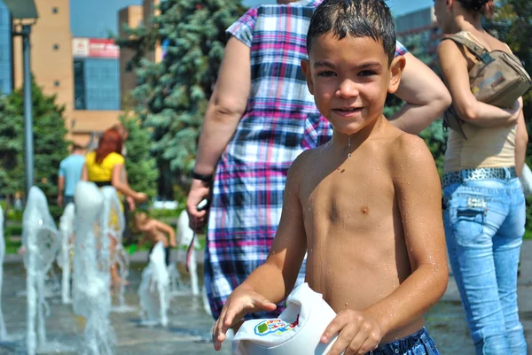 Niño pequeño juega en una fuente de la calle durante las vacaciones —  Fotos de Stock