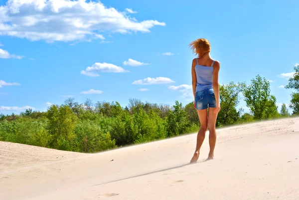Ragazza bionda sessuale in pantaloncini jeans rimane sulla sabbia in una giornata brillante — Foto Stock