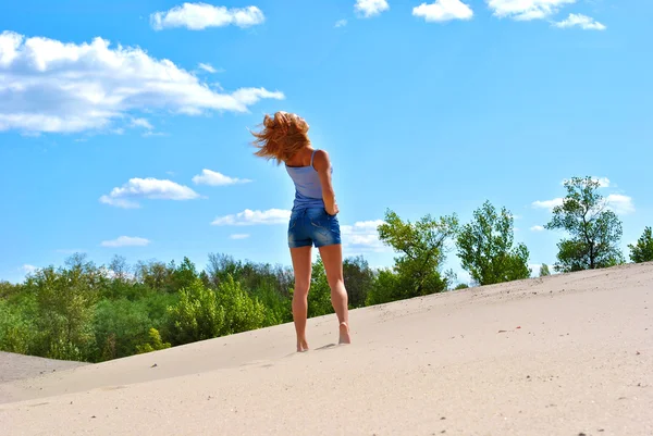 Menina loira sexual em calções jeans fica na areia em um dia brilhante — Fotografia de Stock