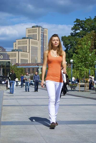 Beautiful red-haired girl in an orange shirt walks in the city on a shiny day — Stock Photo, Image