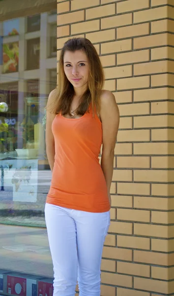 Hermosa chica caucásica pelirroja en una camisa naranja posa cerca de una pared de ladrillo — Foto de Stock