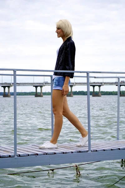 Beautiful blond caucasian model girl in black jacket and jeans poses on the — Stock Photo, Image