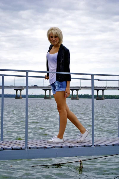 Beautiful blond caucasian model girl in black jacket and jeans poses on the — Stock Photo, Image