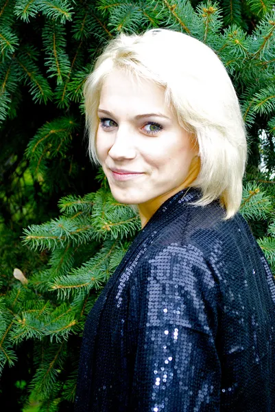 Beautiful blond caucasian model girl poses in front of green fir-tree — Stock Photo, Image