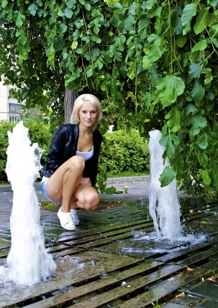 Beautiful blond caucasian model girl poses near small fountain Royalty Free Stock Photos