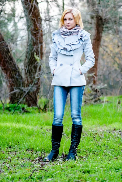 Beautiful blond caucasian model poses in grey coat, jeans and black boots — Stock Photo, Image