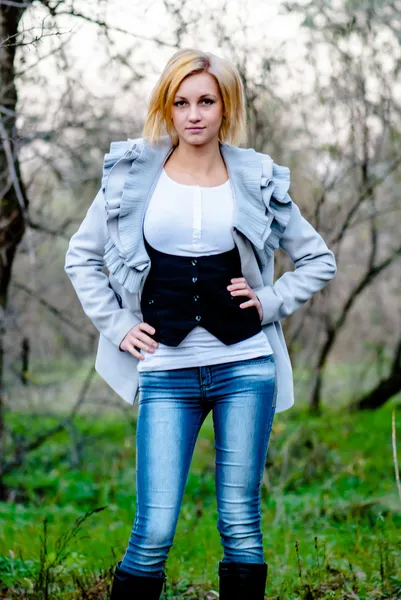Menina bonita posa na floresta em jeans e casaco — Fotografia de Stock