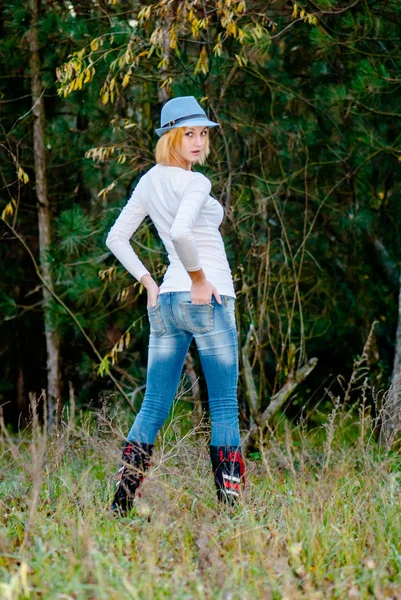 Hermosa giel posa en el bosque en otoño con sombrero de moda y jeans — Foto de Stock