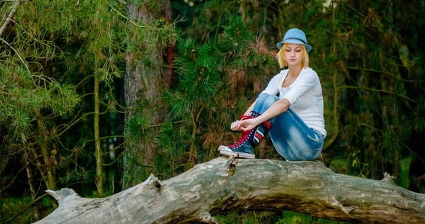 Schöne russische Mädchen sitzt auf dem Baum und posiert mit grauem Hut und Modekleidung — Stockfoto