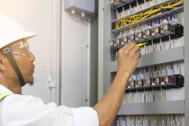 A male electrician works in a control panel with electrical connections connecting devices with a complex working concept tool.