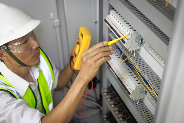 A male electrician works in a control panel with electrical connections connecting devices with a complex working concept tool.