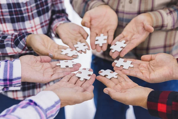 people helping in assembling puzzle, cooperation in decision making, team support in solving problems and corporate group teamwork concept, close up view of hands connecting pieces