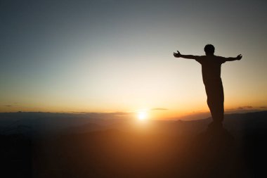 silhouette of man rise hand up praying  on top of mountain and sunset sky abstract background. Freedom and travel adventure concept. 