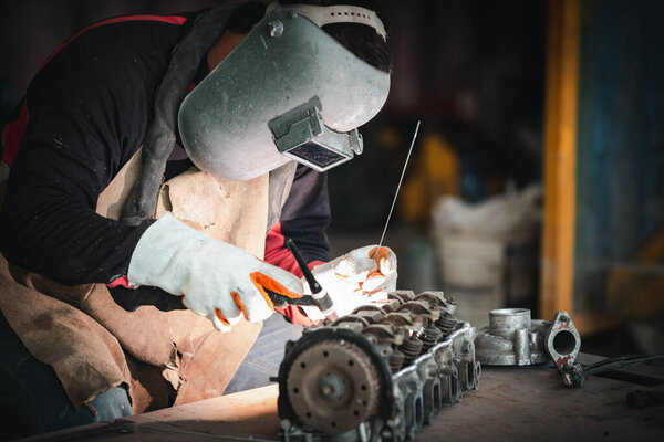 The man in the mask is welding metal with argon-arc.