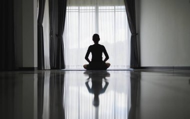 Evde meditasyon yapan genç bir kadının silueti. Erkekler içeride yoga yapıyor. Rahatlama, vücut bakımı, meditasyon, denge, spor, dinlenme konsepti, dua.