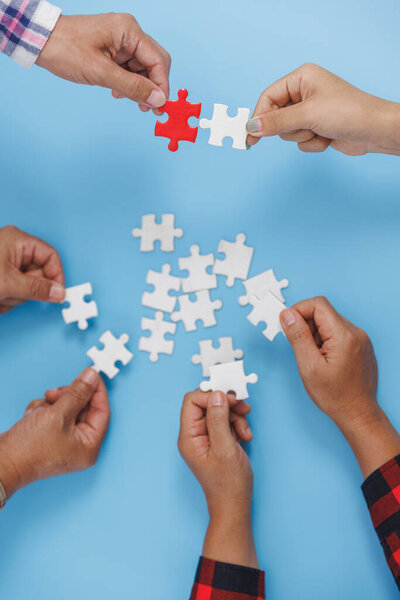 Closeup of businesspeople holding jigsaw puzzle on a blue background. Hand holding the puzzles for the businessmen to work together as a team. Concept of planning work as a teamwork. 
