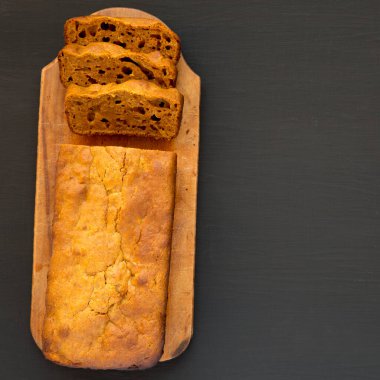 Siyah arka planda, ahşap bir tahtanın üzerinde ev yapımı Balkabağı Ekmeği. Dümdüz, tepeden, yukarıdan. Boşluğu kopyala.