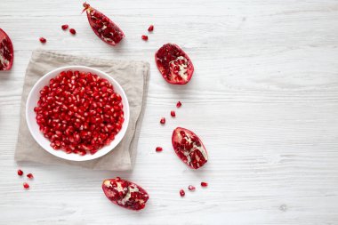 Kırmızı Nar Tohumları, beyaz ahşap bir arka planda bir kasede, üst manzara. Dümdüz, tepeden, yukarıdan. Boşluğu kopyala.