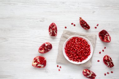 Beyaz ahşap bir yüzeyde, kabın içinde kırmızı nar tohumları, üst manzara. Dümdüz, tepeden, yukarıdan. Metin için boşluk.
